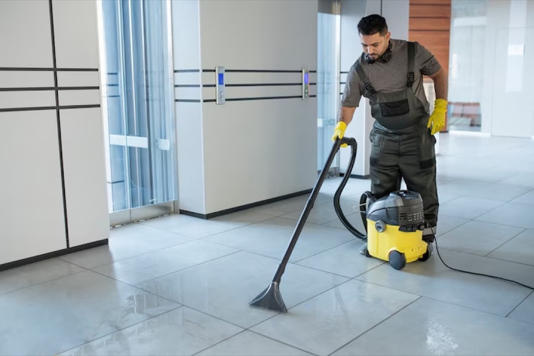 A cleaner using a commercial hot-water extraction machine on the tiled floor of an office foyer.