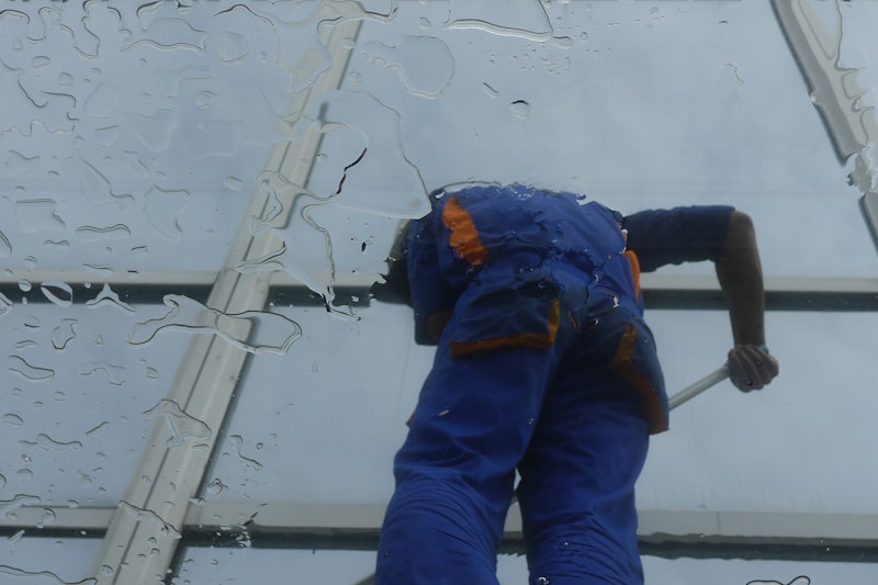 A cleaner in overalls squeegeeing water from a large commercial glass roof.