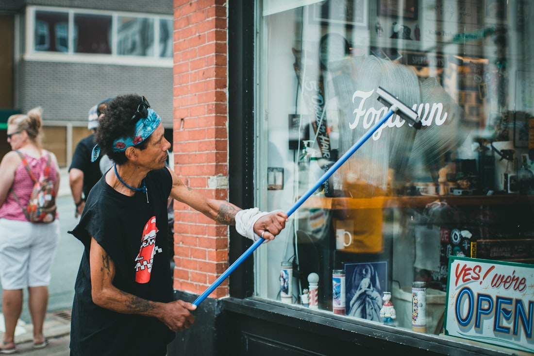 A window cleaner using a squeegee on an extension pole to clean the glass of a shopfront.