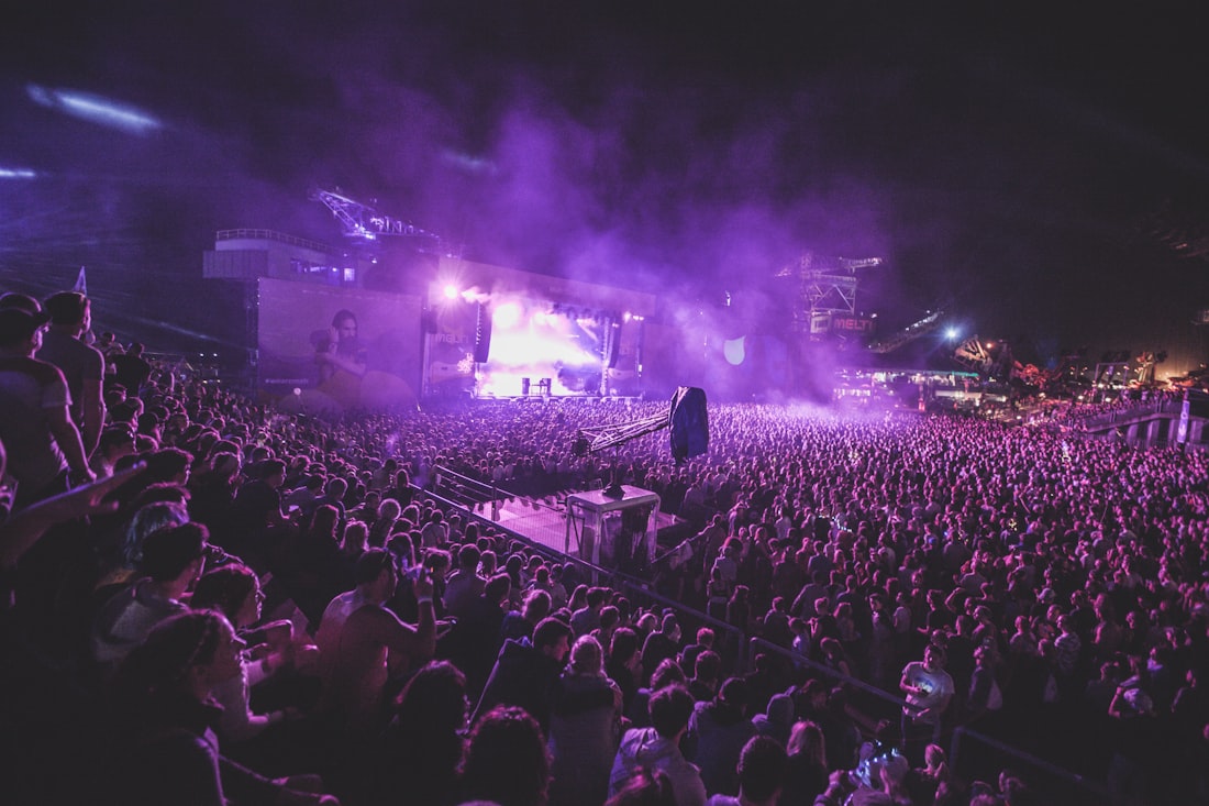 A large crowd of people facing a brightly lit stage at an outdoor evening event.