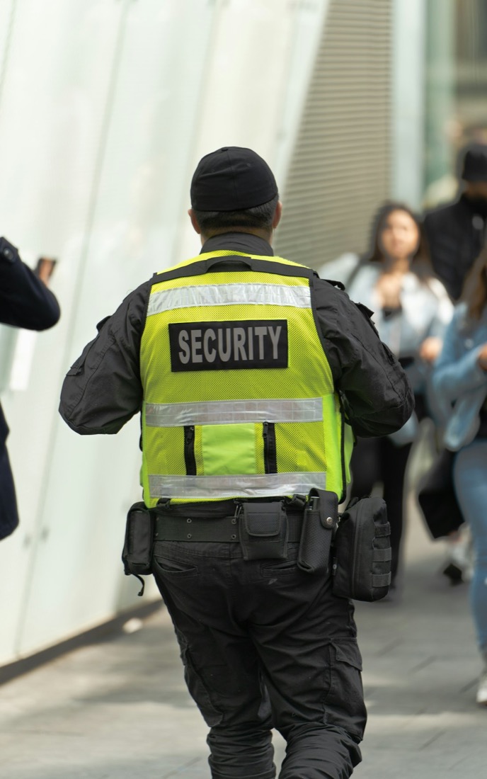 A uniformed security officer in a high-visibility vest marked SECURITY on duty in a busy public area.