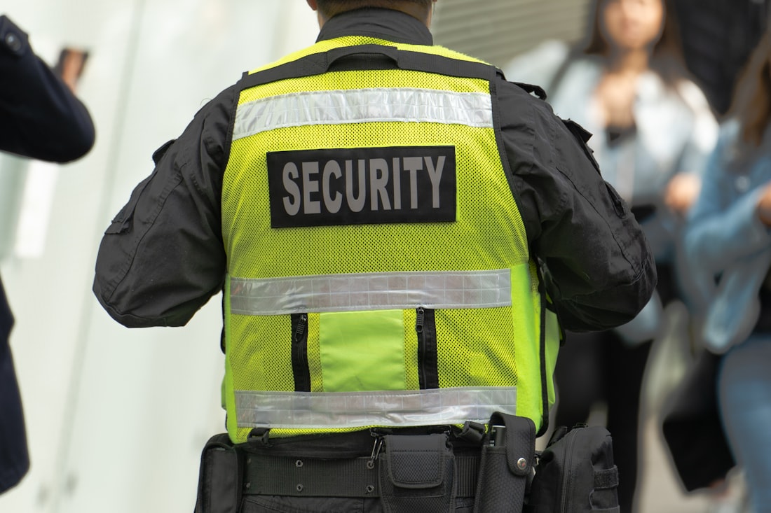 A licensed security guard in a hi-vis SECURITY vest monitoring a busy public area.